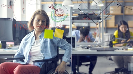 Vrouw in een rolstoel bekijkt informatie op een glazen whiteboard op haar werk