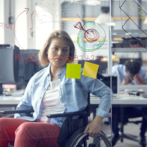 Vrouw in een rolstoel bekijkt informatie op een glazen whiteboard op haar werk